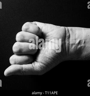 Black & white image of man`s clenched fist and wrist, isolated against a black background with dramatic sidelight Stock Photo